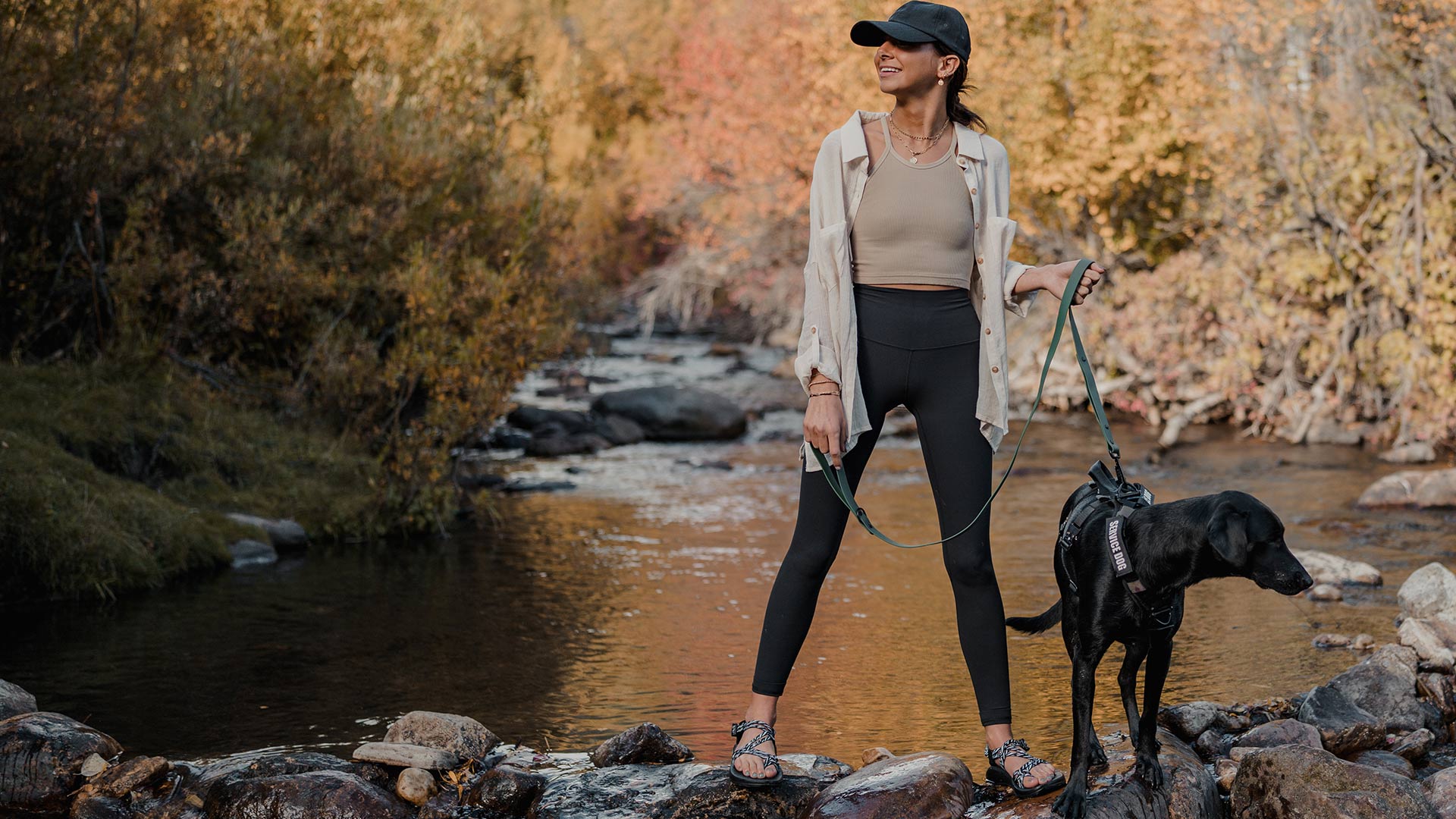 woman walking her black dog in fall season with the sentiero dog leash in woodland green and the extended ascension harness