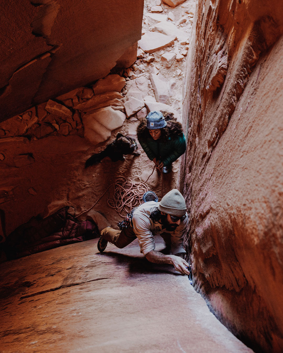 man climbing a crack with a dog sitting at the bottom watching him